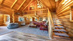 A log cabin interior with a wooden staircase, a leather sofa, and a dining area. - Rowland Log Cabin 3 Bedroom Home by RedAwning (Lyle)