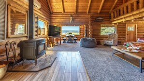 A log cabin interior with a fireplace, wooden furniture, and a view of the outdoors. - Rowland Log Cabin 3 Bedroom Home by RedAwning (Lyle)