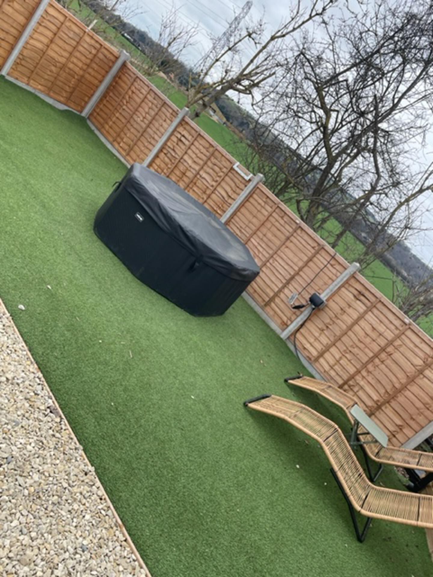 A backyard with artificial grass, a covered barbecue grill, and two wicker chairs.