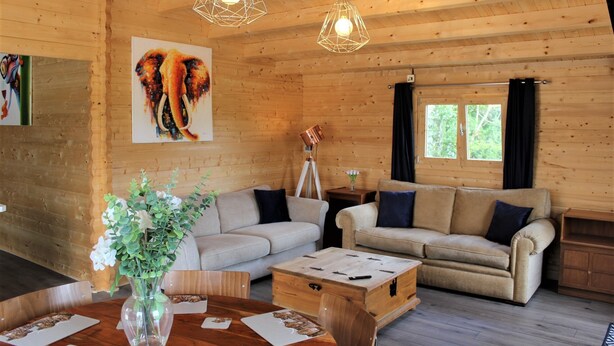 Ein Holzblockhaus-Interieur mit zwei Sofas, einem Esstisch und einem Elefantenbild.