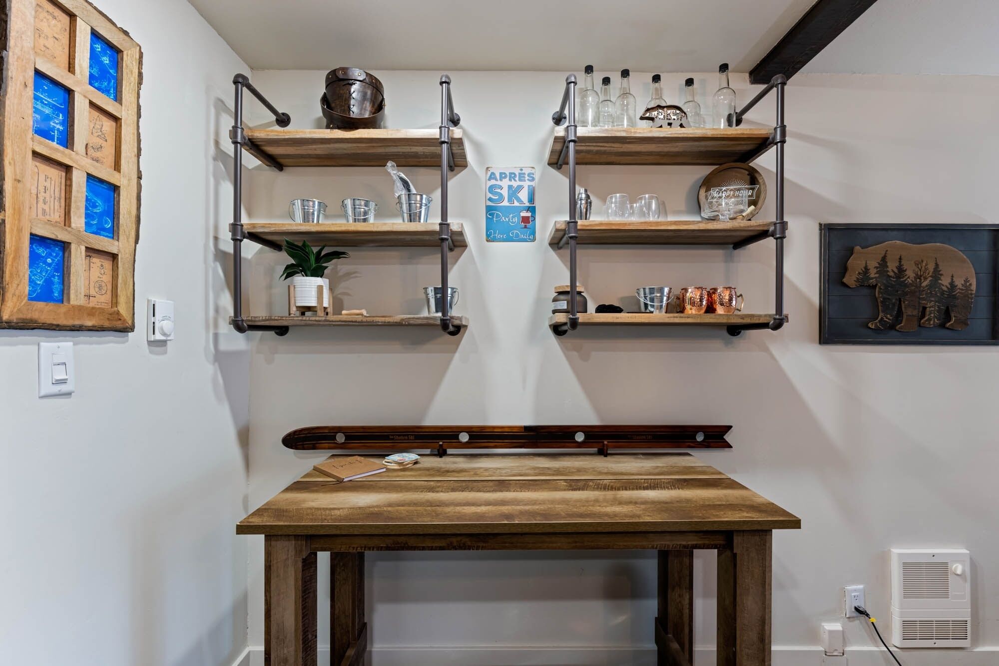 A kitchen with wooden shelves holding kitchenware, a sign reading "APRES SKI Party Here Daily", and a table with a guitar.