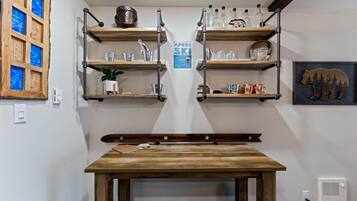 Una cocina con estantes de madera que sostienen utensilios y una mesa con una guitarra.