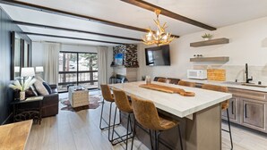 A modern kitchen with a large island, bar stools, a chandelier, and a flat-screen TV. - Luxurious 2 Bedroom Base Camp Condo - Steps from Kirkwood Village 2 Condo by RedAwning (Kirkwood)