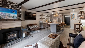 A modern kitchen with a central island, a fireplace, and a dining area with a sofa and chairs. - Luxurious 2 Bedroom Base Camp Condo - Steps from Kirkwood Village 2 Condo by RedAwning (Kirkwood)