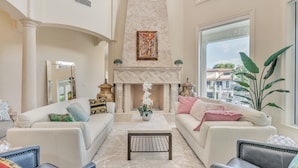 A spacious living room with two white sofas, a marble fireplace, and a large window offering a city view. - Luxury Home Villa D' Amore Southern Florida Paradise Sleeps 10 5 Bedroom Villa by RedAwning (Fort Lauderdale)
