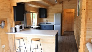 Innenansicht einer Holzhütte mit Küchenzeile, inklusive Kochinsel, Barhocker, Kühlschrank und Spüle.