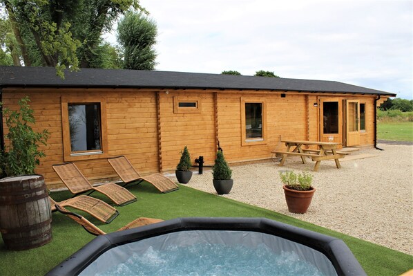 A wooden cabin with a hot tub, lounge chairs, and a picnic table.