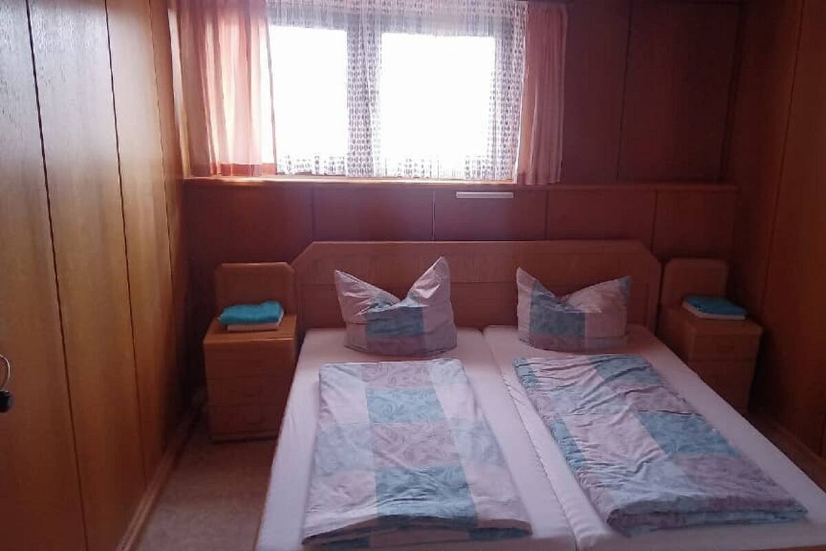 Een kleine, gezellige slaapkamer met een enkel bed, twee nachtkastjes en een raam met gordijnen.