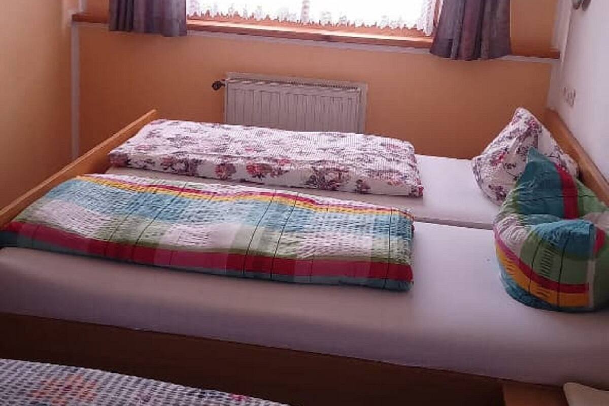Een knus kamertje met een enkel bed, een raam met gordijnen en een radiator.