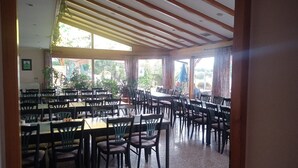 Uma sala de jantar espaçosa com várias mesas e cadeiras, grandes janelas com cortinas e um teto com vigas de madeira.