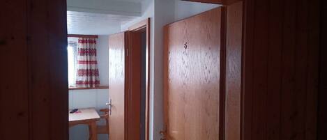 A wooden door with a brass handle, leading to a room with a white ceiling and a window with a red and white patterned curtain.