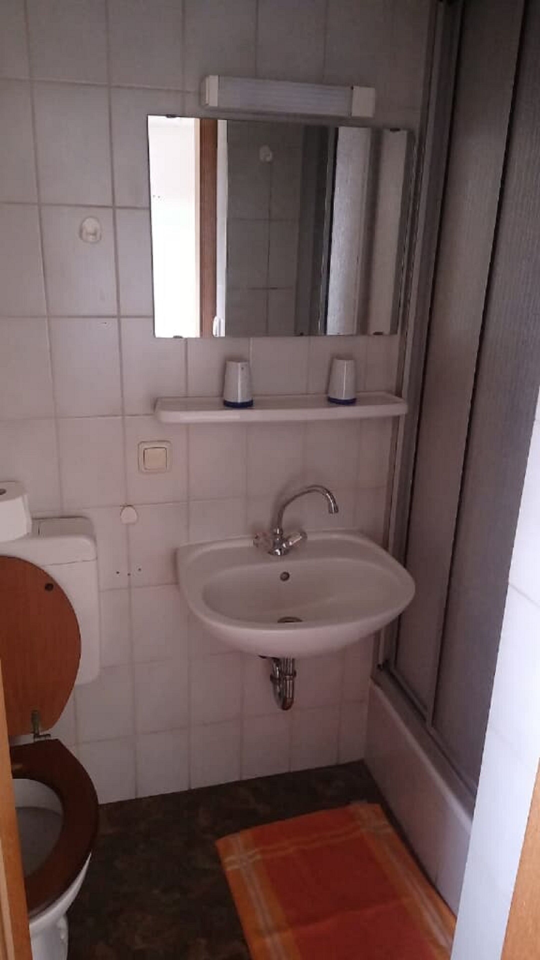 Un baño con lavamanos blanco, un espejo encima y un inodoro.