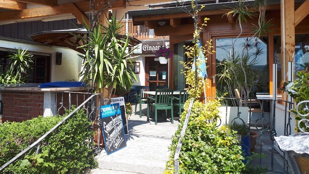Um edifício com fachada de madeira, um letreiro com a palavra 'Ginger', área de estar externa e vasos de plantas.