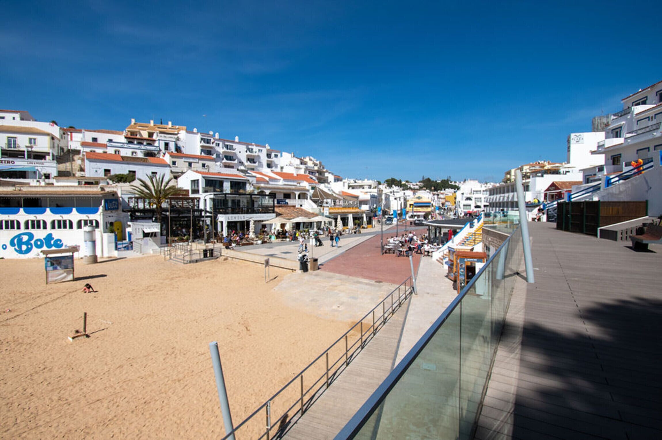 Une ville côtière dotée d’une plage de sable, d’une promenade et de bâtiments blancs aux toits orange.