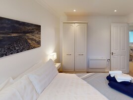 Un dormitorio con una cama, una mesita de noche con lámpara, un armario y un cuadro en la pared.