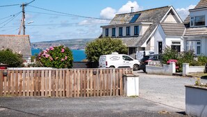 A coastal property with a white van parked in front, a wooden fence, and a view of the sea. - Suncroft (Port Isaac)