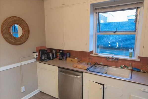 A compact kitchen with a dishwasher, a window with a view, and a round mirror on the wall.