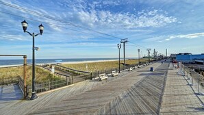 A wooden boardwalk with railings, street lamps, and a view of the beach and ocean. - Beach Block Retreat w/Patio, Off Street Parking, Linens & Towels, Beach Gear (Seaside Heights)