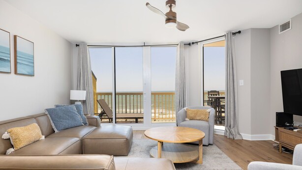 Un salon moderne avec un canapé, un fauteuil et une table basse ronde, un téléviseur et un balcon offrant une vue agréable.