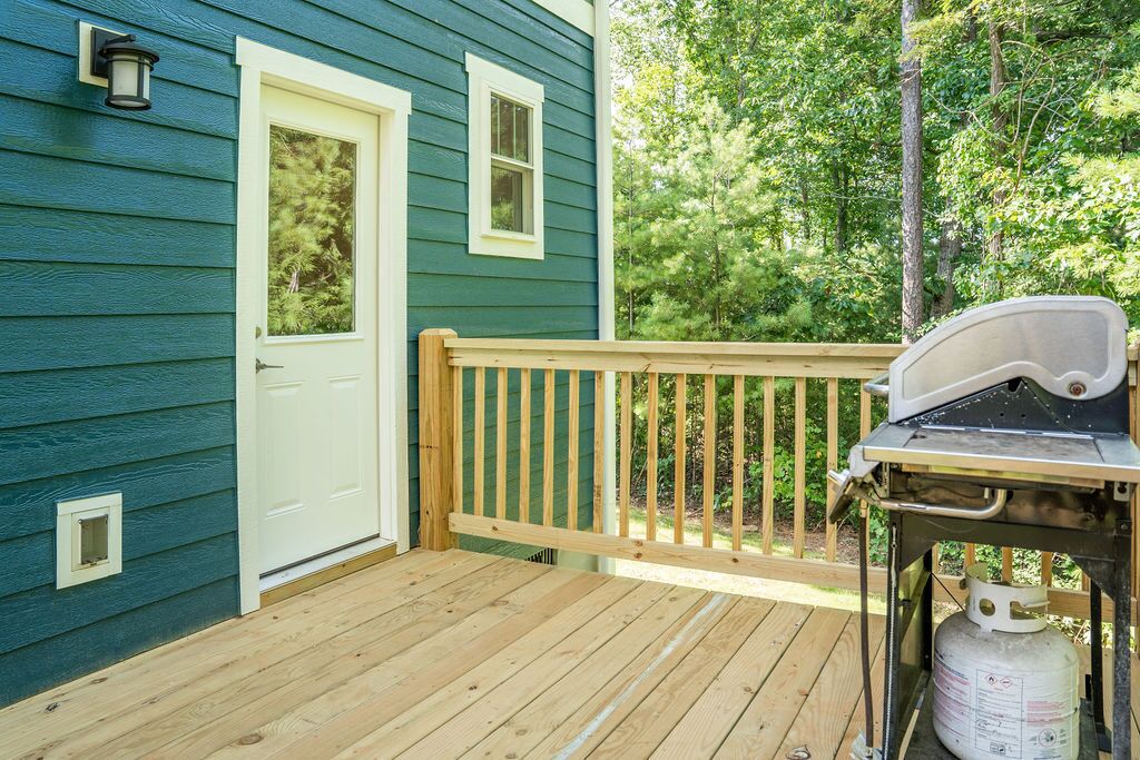A wooden deck with a gas grill and propane tank, a white door, and a small window.