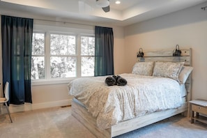 A bedroom with a large bed, a bedside table, a chair, and a window with curtains.