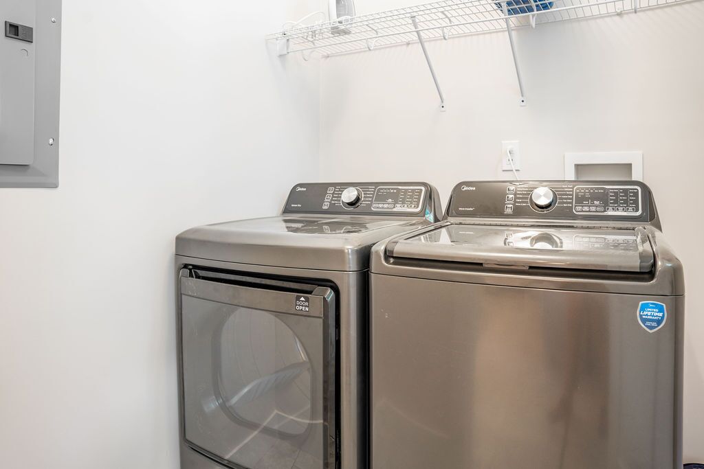 A laundry room with two front-loading washing machines and a metal shelf above.