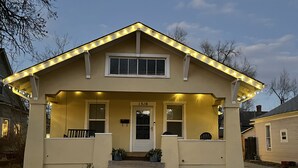 A two-story house with a front porch, a number '13' on the door, and string lights on the roof. - Cheerful 3-bedroom minutes from downtown and OCC (Colorado Springs)
