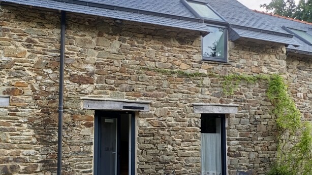 Un edificio de piedra con techo inclinado, dos puertas y una pequeña mesa con sillas afuera.