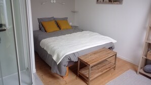 Un dormitorio con una cama, un banco de madera, una mesita y un estante en la pared.
