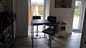 Cocina compacta con comedor, microondas, cafetera y mesa con sillas.