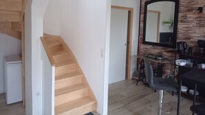 Una cocina moderna con una escalera de madera, un comedor con una mesa y sillas negras, y un espejo grande en la pared.