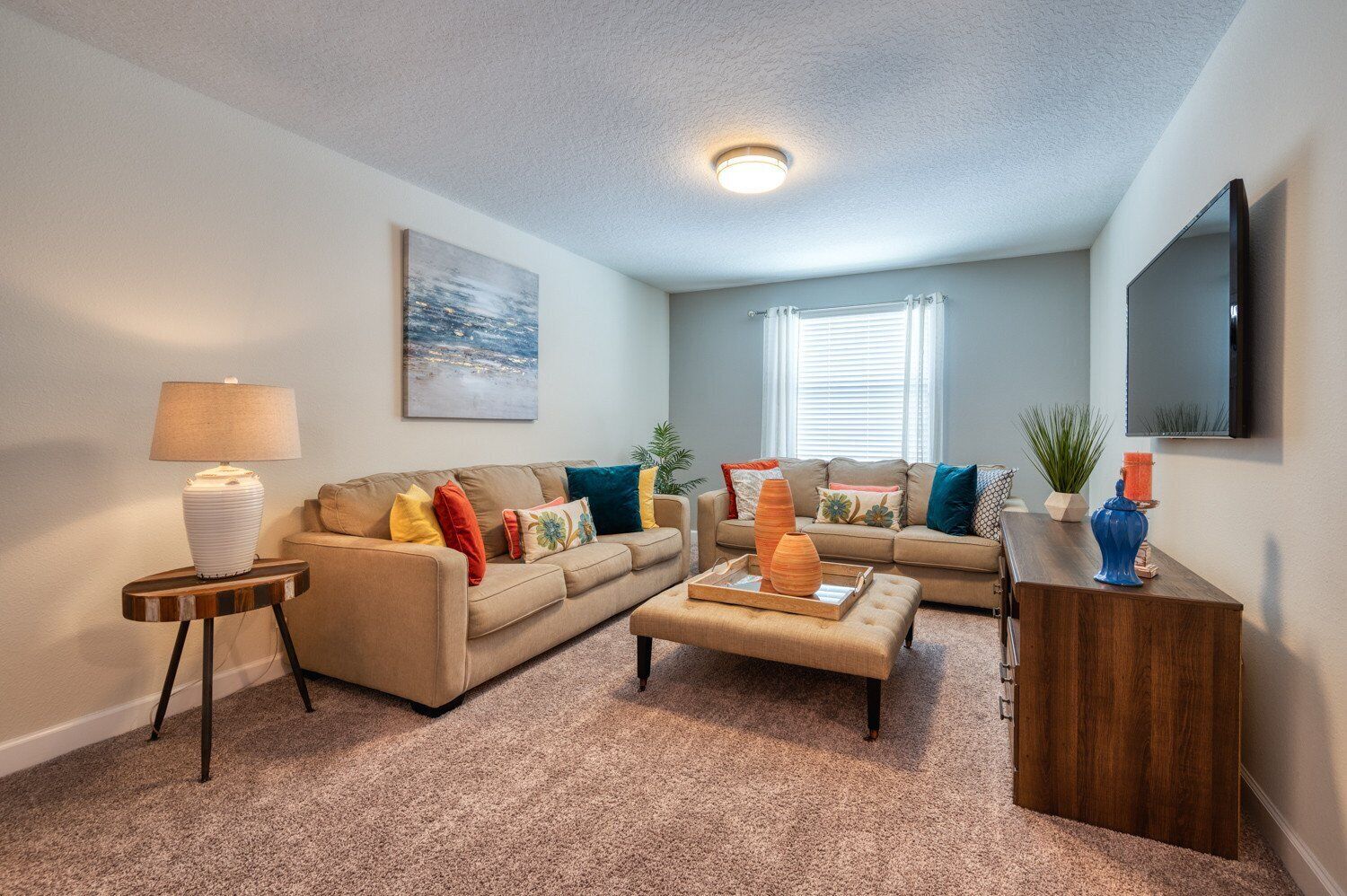 A living room with a beige sofa, a coffee table, a lamp, and a TV on a wooden stand.