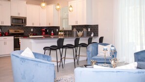 A modern kitchen with white cabinets, a central island with bar stools, and pendant lighting. - Last Minute Disney! Private Pool, Hot Tub, Game Room & Themed Bedrooms. Book Now! #32862 (Orlando)