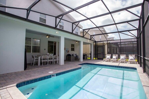 Une piscine extérieure couverte, dotée d’un espace patio, de chaises longues et d’un coin repas.
