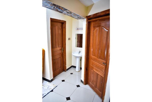 A narrow hallway with wooden doors and a white tiled floor.