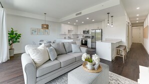 A modern living room with a grey sofa, a coffee table with a tray of flowers, and a dining area with a white table and chairs. - All-New, Waterfront Condo Near Downtown Sarasota (Sarasota)