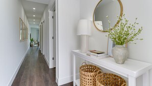A hallway with a white console table, a mirror, a lamp, and a vase with flowers. - All-New, Waterfront Condo Near Downtown Sarasota (Sarasota)