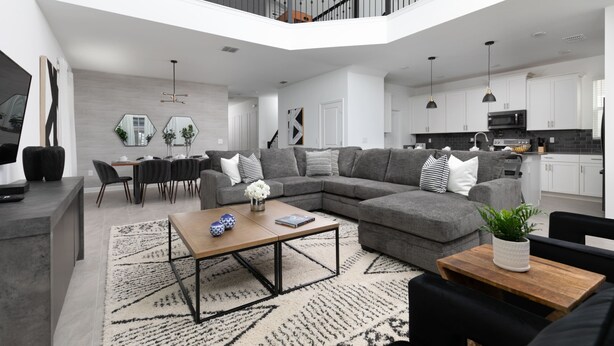 Ein modernes Wohnzimmer mit einem grauen Ecksofa, einem Couchtisch und einem Essbereich mit weißem Tisch und Stühlen.