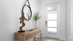 Ein Holzkonsolentisch mit Spiegel und Dekoration, eine Tür mit satinierten Glasfeldern und ein gemustertes Teppich auf Fliesen.