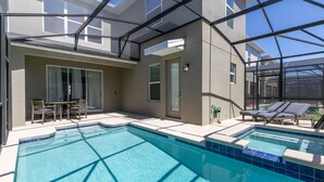 Ein Pool mit Glasveranda, einem Tisch mit Stühlen und Liegestühlen.