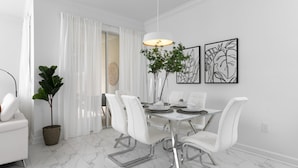 A modern dining area with a white table, chairs, and a hanging light fixture.