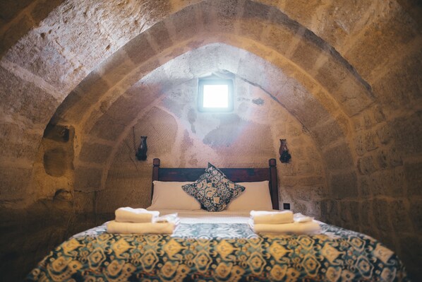 A room with a stone arch ceiling, a bed with patterned bedding, and a pillow with a geometric design. - Tale Cave INN (Ürgüp)