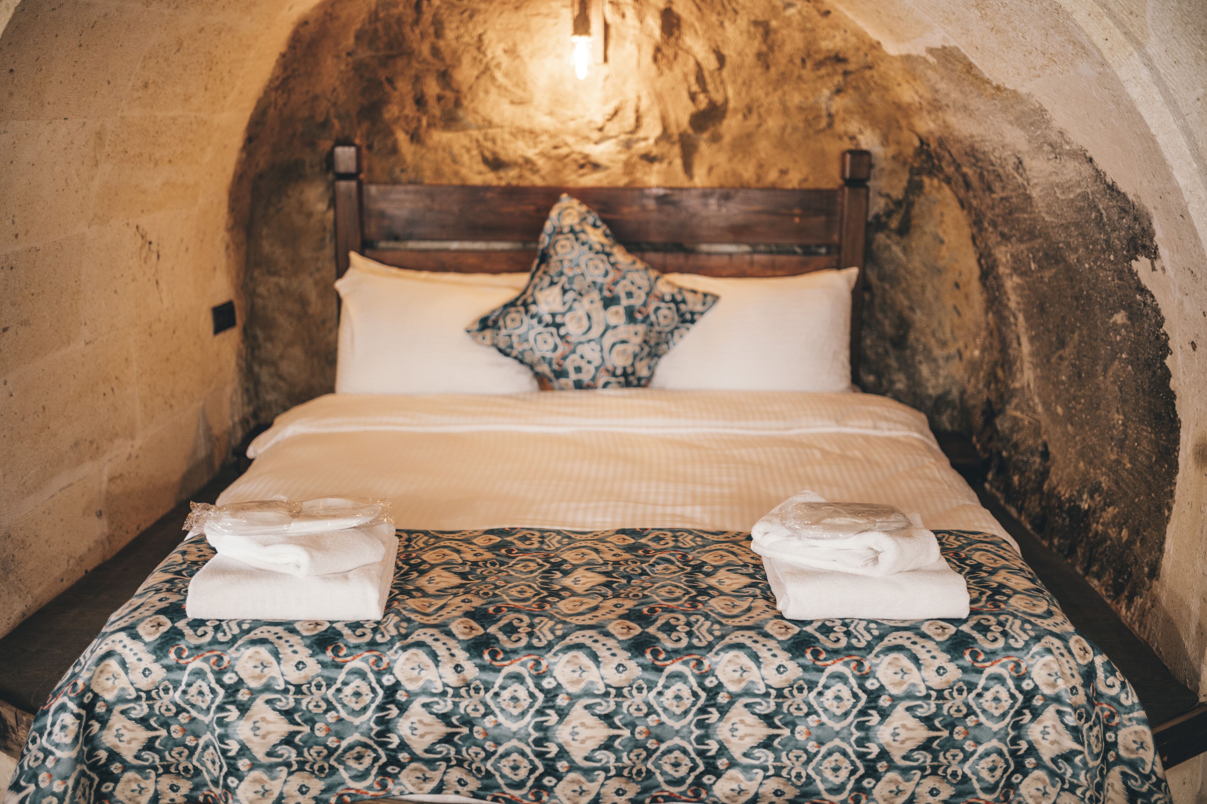 Una cama con un edredón estampado, una almohada y dos toallas dobladas.