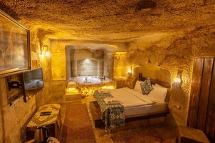 A cozy, cave-like bedroom with a bed, a small table with a kettle, and a television mounted on the wall.