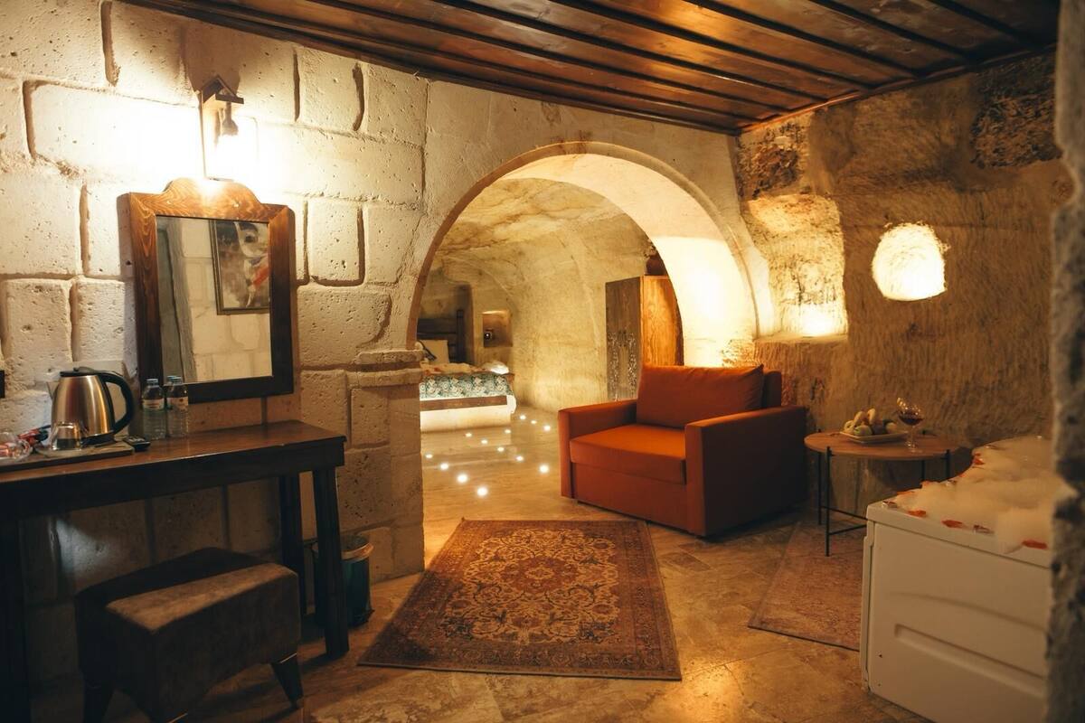 Una habitación acogedora con pared de piedra, un escritorio de madera, un sofá rojo y una pequeña mesa con una copa de vino.