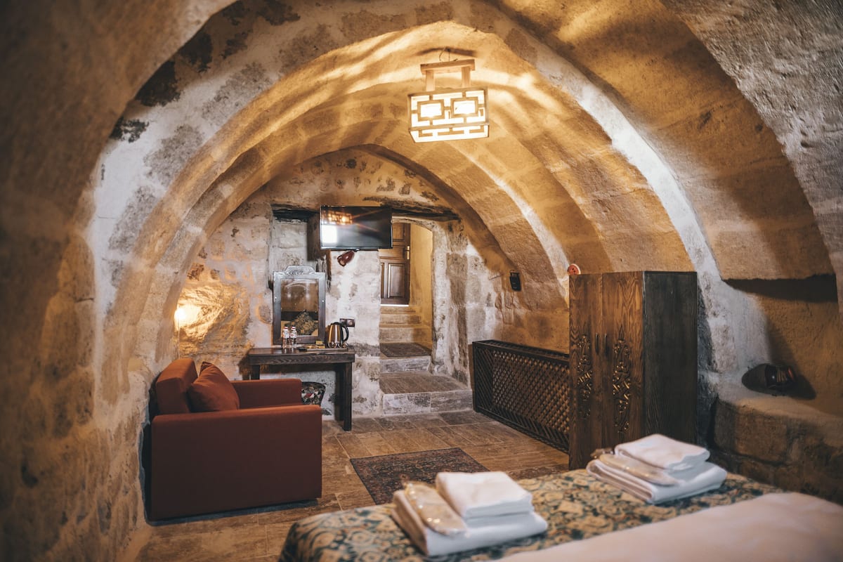 Una habitación acogedora con paredes de piedra, un sofá, una cama con toallas ordenadas y un televisor al fondo.