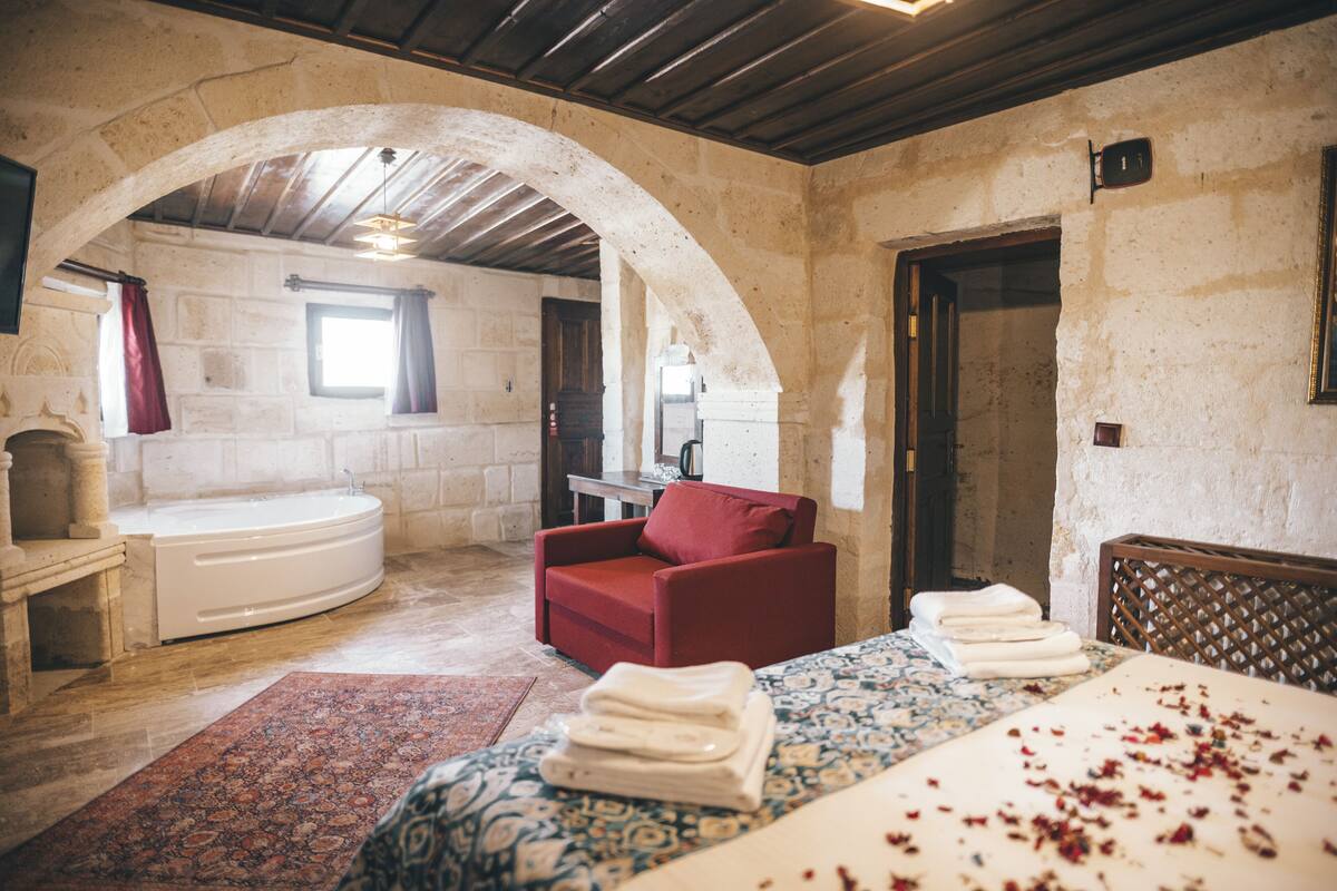 Una habitación con una cama, una silla roja, una bañera y un arco de entrada.