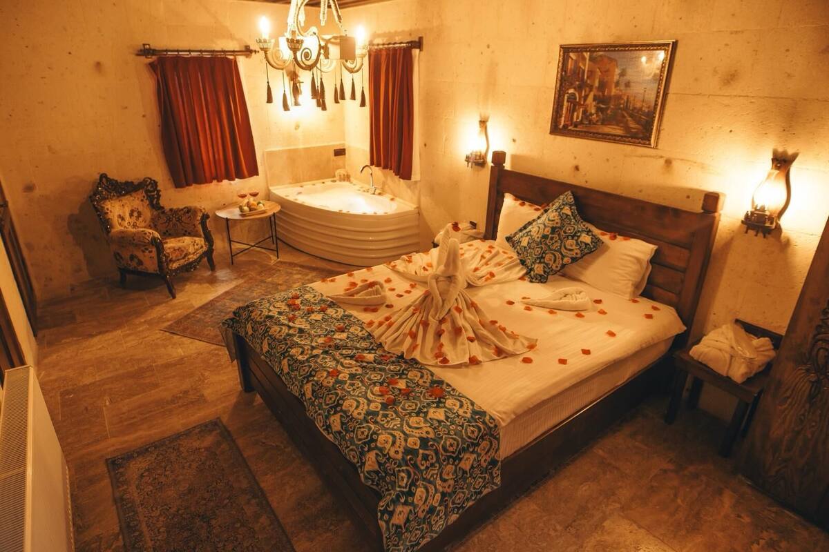 Un dormitorio con una cama grande, una zona de estar con una silla, una mesita, una bañera y una araña.