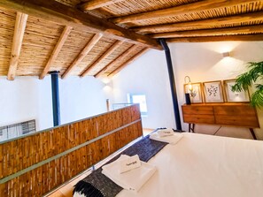 A hotel room with a wooden ceiling, a bed with white linens, a wooden dresser, and a wall-mounted light fixture.