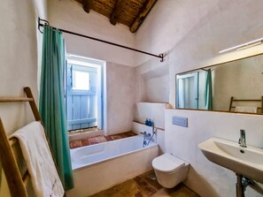 A bathroom with a bathtub, toilet, sink, and a window with curtains.
